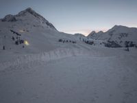 a mountain is shown at dusk, with a ski slope and a line of trees visible