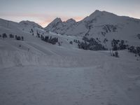 a mountain is shown at dusk, with a ski slope and a line of trees visible