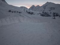 a mountain is shown at dusk, with a ski slope and a line of trees visible