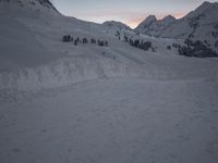 a mountain is shown at dusk, with a ski slope and a line of trees visible