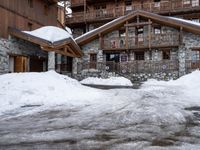 a lot of snow in front of a lodge building by a road with stairs up