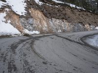 a steep cliff with a sloped off section on the side next to it, has snow piled around it