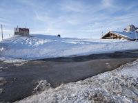 a pile of snow and water in front of an alpine lodge with a snow covered slope behind it