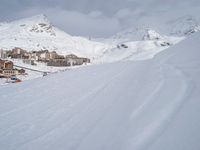 a skier going down a snowy slope by an alpine resort in winter attire with skis and poles