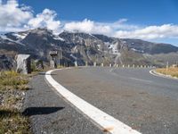 an empty road surrounded by mountains and clouds in the background with white markings on the street