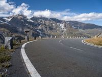 an empty road surrounded by mountains and clouds in the background with white markings on the street