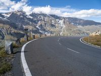 an empty road surrounded by mountains and clouds in the background with white markings on the street