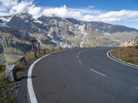 an empty road surrounded by mountains and clouds in the background with white markings on the street