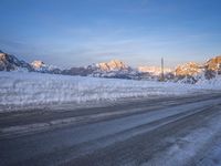 a lone road with snow and ice on both sides and a mountain range in the back