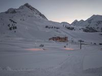 a ski lodge at sunset on a mountain with snow in front of it and a ski lift at the top of a slope