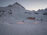a ski lodge at sunset on a mountain with snow in front of it and a ski lift at the top of a slope