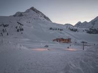 a ski lodge at sunset on a mountain with snow in front of it and a ski lift at the top of a slope