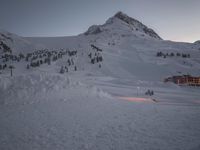 a ski lodge at sunset on a mountain with snow in front of it and a ski lift at the top of a slope