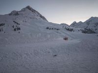 a ski lodge at sunset on a mountain with snow in front of it and a ski lift at the top of a slope