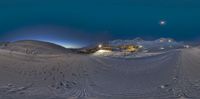 a ski slope with several tracks and buildings in the distance at night time, seen from the bottom