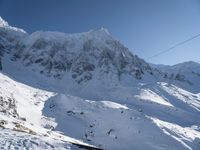 skiers ride along a ski slope in the snow with mountain range in background and power lines above