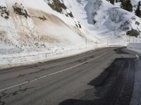 a snowy mountain road with a snowbank below it and trees near the mountainside
