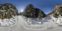 a person skis down a snow covered mountain side path with sun beaming through the sky