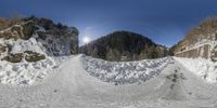 an image of a snow covered mountain road with a bright sun in the background and some trees and grass on the opposite side of it