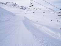 snow covered slope in the middle of a ski area as people ski on it near ski lift