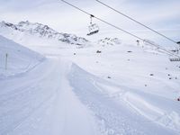 snow covered slope in the middle of a ski area as people ski on it near ski lift