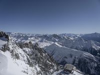 a group of skiers with snowboarders standing on a steep mountain side looking out over a valley