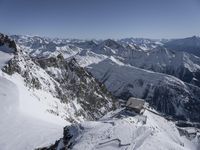 a group of skiers with snowboarders standing on a steep mountain side looking out over a valley