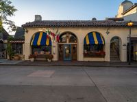 there is a yellow building with blue awnings, a green door and red shutters