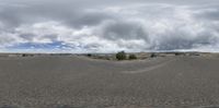 a cloudy sky over a desert area with a street and trees in front of it