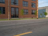 an empty street in front of a large red brick building on the other side of the road is a street light that has a line for motorists