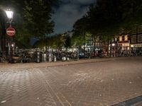 a city square with lots of bicycles parked by the fence and buildings in the background