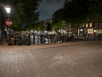 a city square with lots of bicycles parked by the fence and buildings in the background