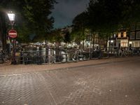 a city square with lots of bicycles parked by the fence and buildings in the background