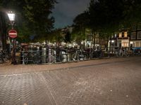 a city square with lots of bicycles parked by the fence and buildings in the background