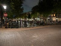 a city square with lots of bicycles parked by the fence and buildings in the background