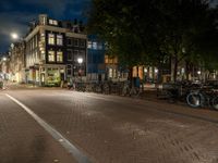 bicycles are parked on the sidewalk by a building in front of trees and buildings in the dark at night