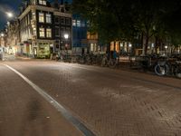 bicycles are parked on the sidewalk by a building in front of trees and buildings in the dark at night