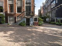 a brick paved area with stairs and a building in the background and some bushes in front of it