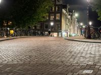 people are walking down the sidewalk in the city at night time with several bicycles parked beside them