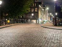 people are walking down the sidewalk in the city at night time with several bicycles parked beside them