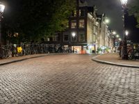 people are walking down the sidewalk in the city at night time with several bicycles parked beside them