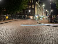 people are walking down the sidewalk in the city at night time with several bicycles parked beside them