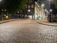 people are walking down the sidewalk in the city at night time with several bicycles parked beside them