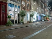 a brick road with two bicycles parked along it at night, on the side of the street is a brick building with windows and a bicycle sign in the middle