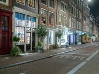 a brick road with two bicycles parked along it at night, on the side of the street is a brick building with windows and a bicycle sign in the middle