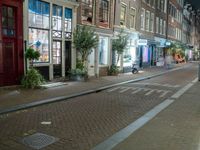 a brick road with two bicycles parked along it at night, on the side of the street is a brick building with windows and a bicycle sign in the middle