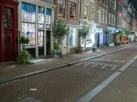 a brick road with two bicycles parked along it at night, on the side of the street is a brick building with windows and a bicycle sign in the middle