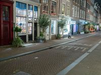 a brick road with two bicycles parked along it at night, on the side of the street is a brick building with windows and a bicycle sign in the middle