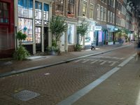 a brick road with two bicycles parked along it at night, on the side of the street is a brick building with windows and a bicycle sign in the middle