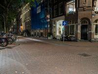 two bikes parked on the sidewalk next to some building by street lamps at night at night